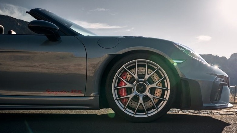 close-up of the front wheel of a gray 718 Spyder RS parked on asphalt in front of a partially cloudy sky