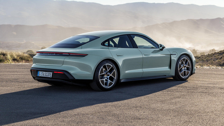 Rear 3/4 view of the Porsche Taycan parked on a paved surface with hills and mountains in the background