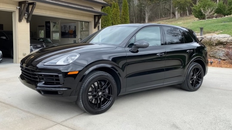 Driver's side 3/4 view of a black 2021 Porsche Cayenne parked in a driveway in front of a building