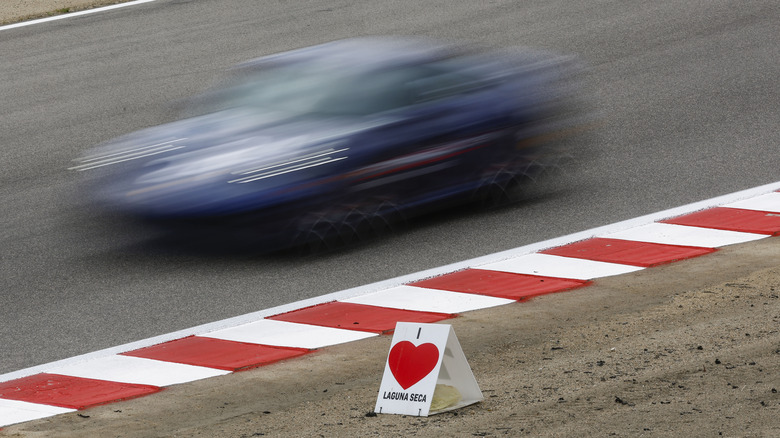 A blue Porsche 911 speeding by a sign at Laguna Seca