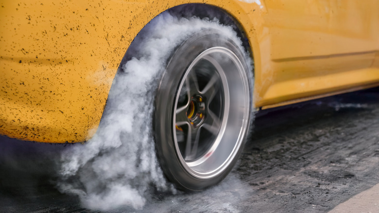 A yellow muscle car with a tire doing a burnout