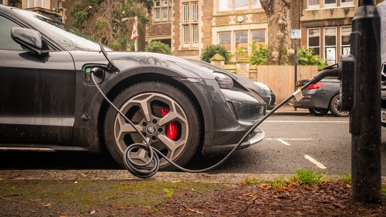 A achromatic Porsche Taycan charges via a thoroughfare lamp successful London