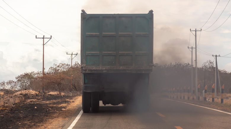 Rear view of a dump truck on a road spewing thick clouds of black smoke