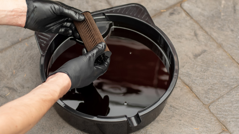 Used motor oil in a black tray and used oil filter after a DIY oil change