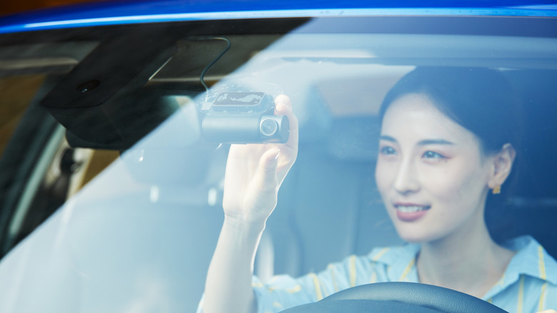 A lady adjusting a dashcam on a car windshield