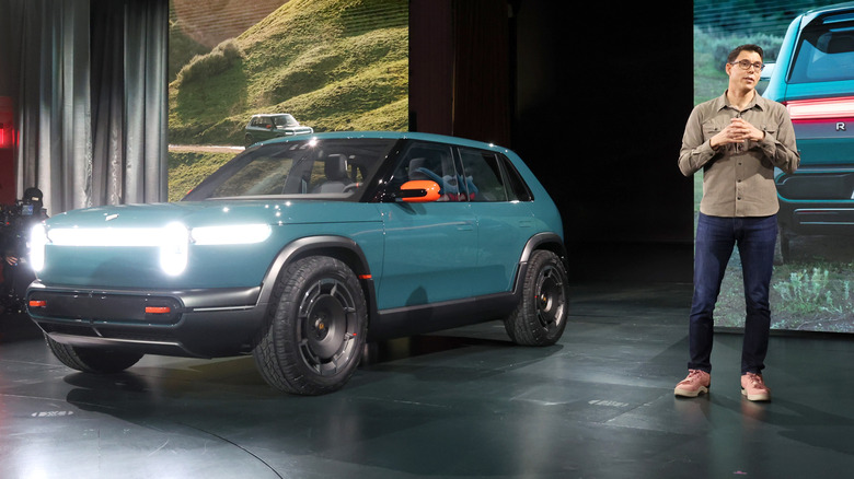 A Rivian R3 displayed at a conference as a man speaks.