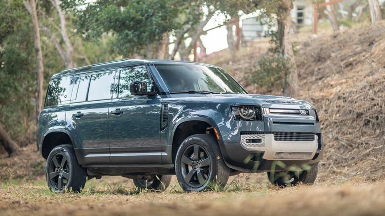 a blue Land Rover Defender 110 parked on grass with its air suspension lifted