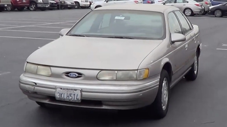 A Ford Taurus sits in a parking lot with other cars in the background.