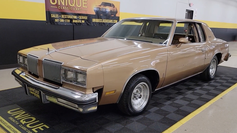 A tan Cutlass Supreme sits parked indoors.