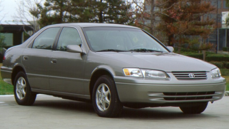 A 1997 Toyota Camry sits parked in front of trees and a building.