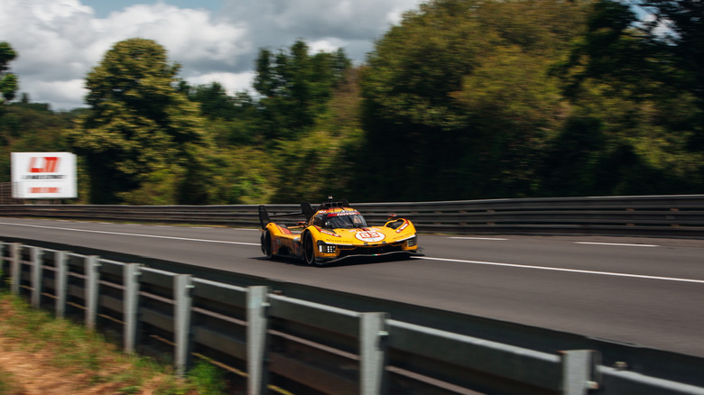 a yellow race car driving on a track with woods in the background