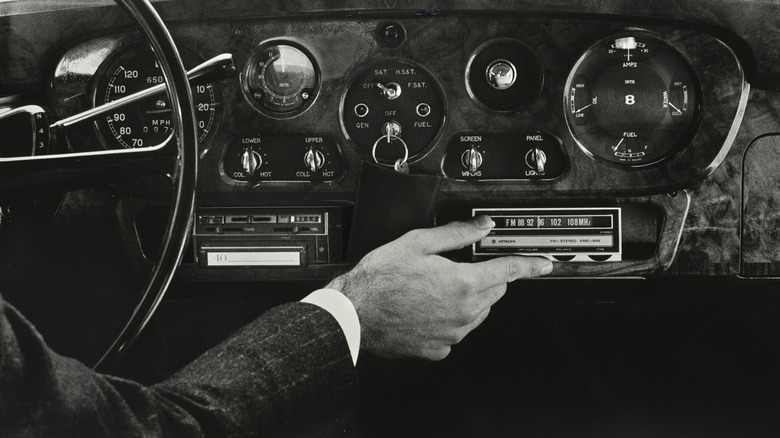 An old car dashboard with the driver tuning a radio