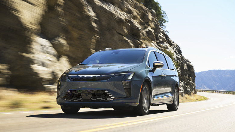 Front three-quarters shot of a gray Chrysler Pacifica driving on a mountain road past a rocky mountainside