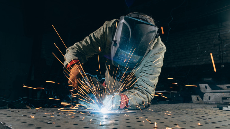 A person welding while wearing a mask, with sparks flying.