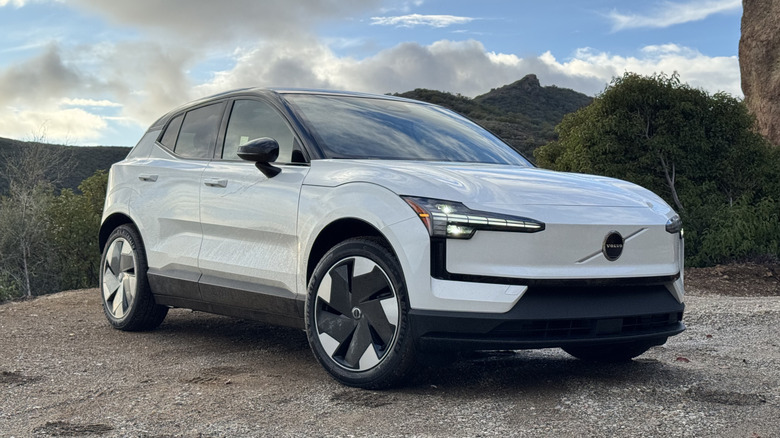 A front three quarters shot of the white EX30 parked on dirt in front of clouds and mountains