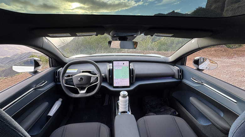 A photo looking forward from the rear seats showing the EX30s artful dashboard with a sunset and some mountains out the windows