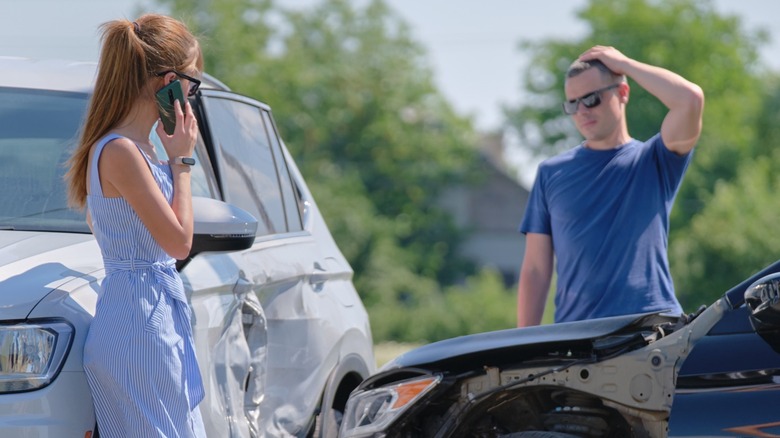 A woman and a man standing by their cars after an automobile accident.