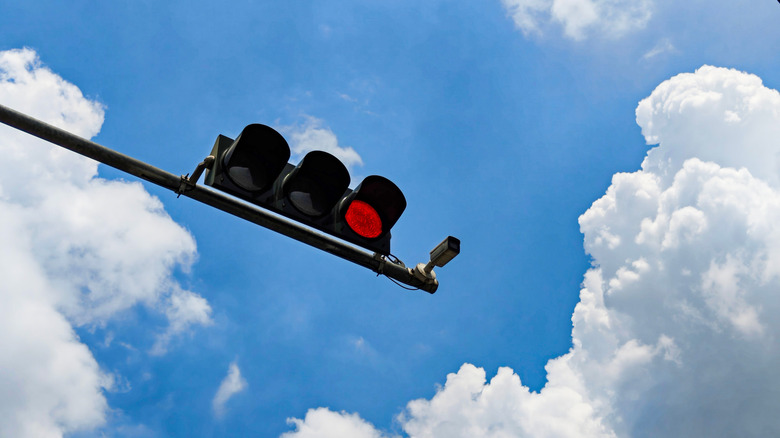 A security camera and a traffic light showing a red signal, mounted on the same metal pole, against a clear blue sky.