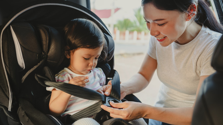 a little kid gets put into a car seat by their mom