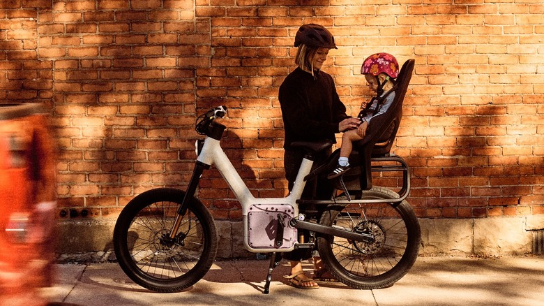 A woman readies her toddler for a ride on an Also TM-B fitted with a child seat