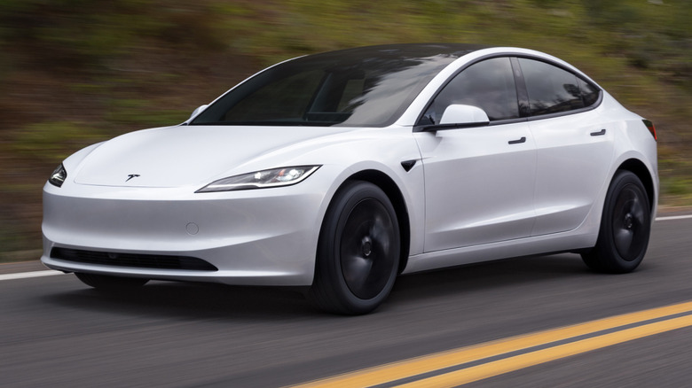 White Tesla Model 3 driving down a paved road with double yellow lines