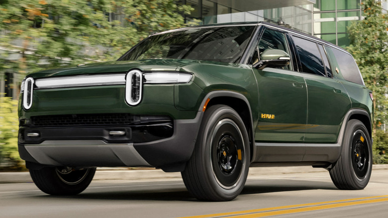 A green Rivian R1S SUV driving down a city street next to modern buildings