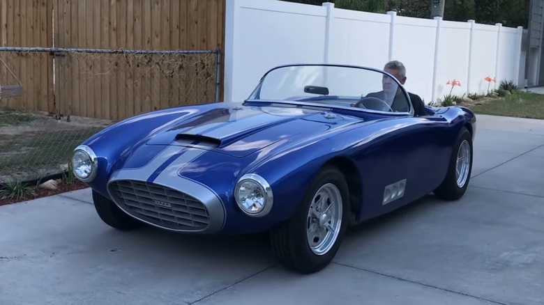 A 1957 Byers SR-100 sports car being driven down a driveway by a man.