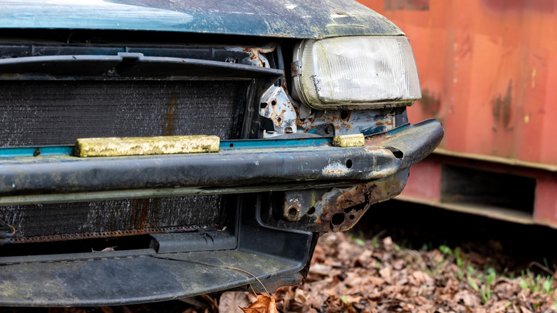 A green car without a front bumper that looks like it's been sitting for a while.