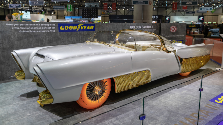 The Golden Sahara II, a gold-trimmed white 1950s custom convertible with glowing tires, on display at a motor show