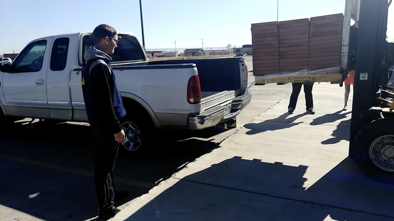 a man stands waiting for a huge load of bricks to ruin his truck's suspension