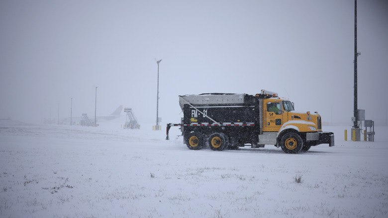 a dump truck full of road salt sits in an empty parking lot on a snowy day