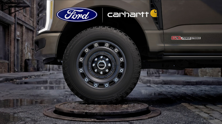A photo of the front wheel of a brown Ford Super Duty Carhartt truck stopped on a manhole cover with a Ford and Carhartt logo on top of it