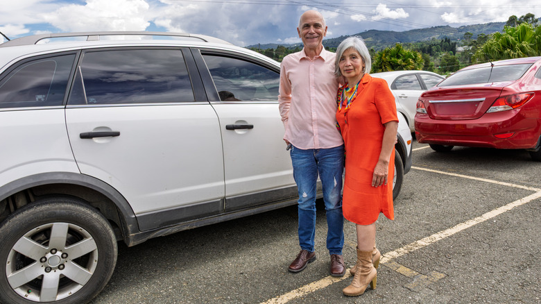 two older people stand in front of their SUV.