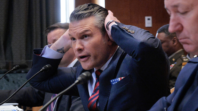 Pete Hegseth smooths his hair at a hearing