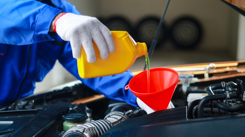 Technician refilling a car's engine oil using a funnel