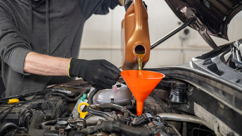 A mechanic pouring oil into a car engine using a funnel