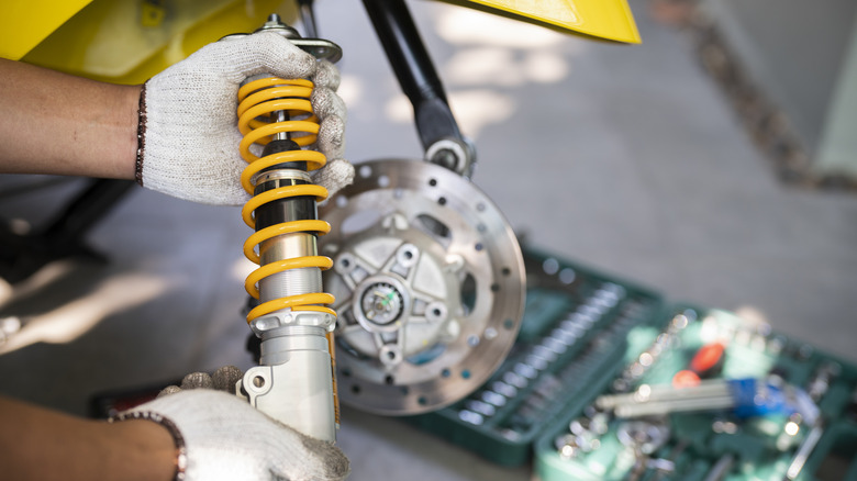 An auto mechanic holds a shock absorber during a repair