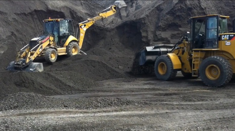 Backhoe loosens pile of recycled asphalt millings