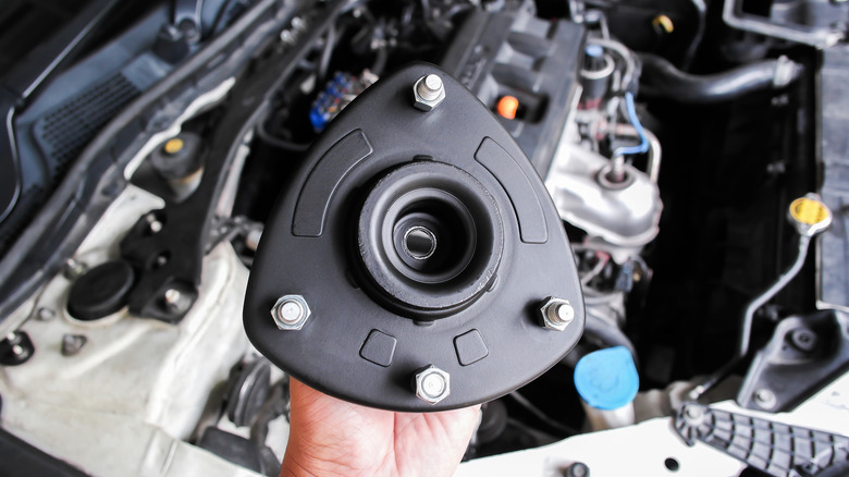 A mechanic holding a strut mount with the engine bay in the background