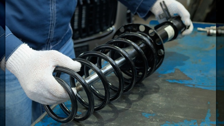 A technician inspecting a vehicle strut on a workbench.