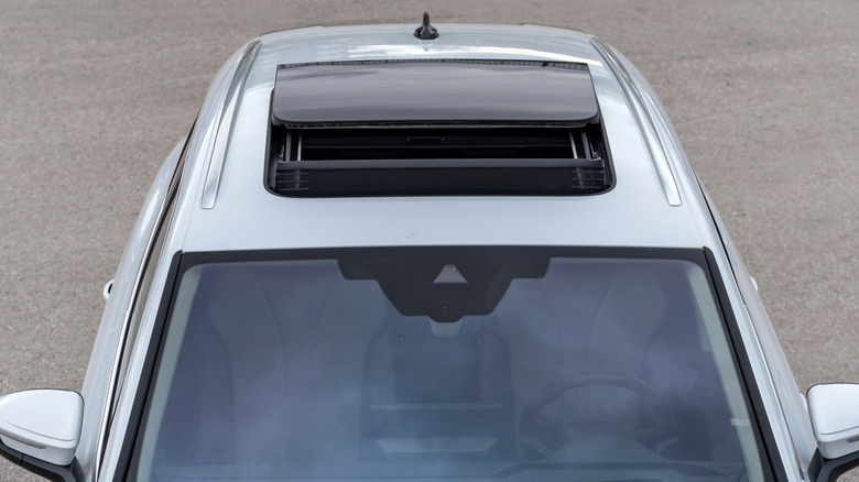 A silver gray car in a parking lot with an open sunroof