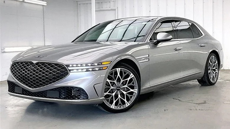 Front three quarters shot of a Savile Silver Genesis G90 parked on concrete in a white-walled room