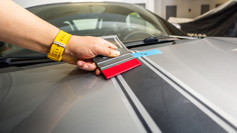 A hood stripe decal being applied on a car with the help of a squeegee.