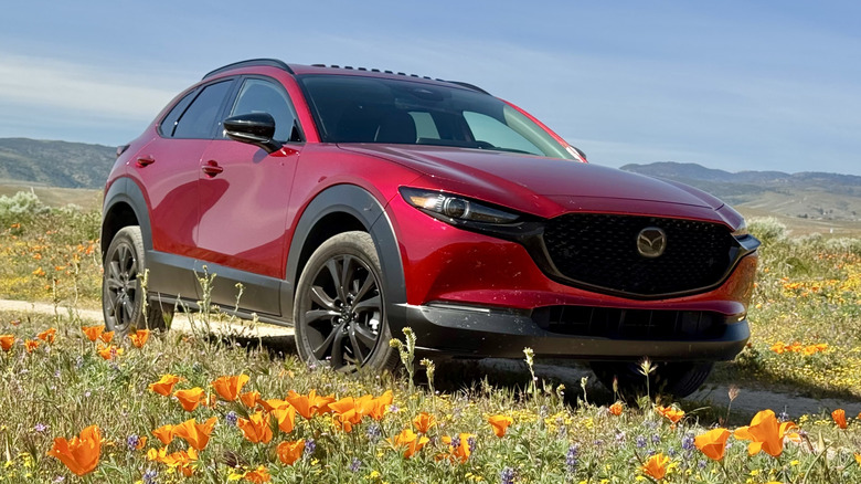 A front three-quarters shot of the red CX-30 parked on a dirt trail behind blooming California Poppys and in front of a blue sky