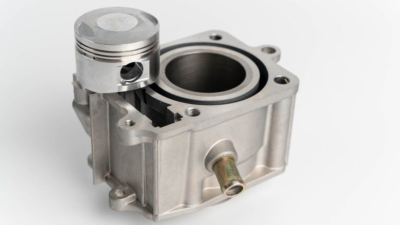 A small piston rests on a single cylinder engine block against a white background