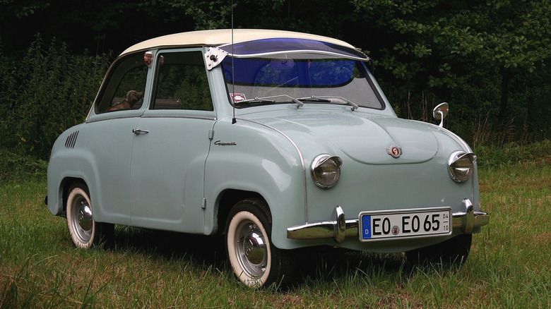 A light-blue Goggomobil sedan with an exterior blue sun visor parked in a grassy area.