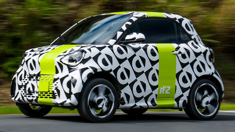 A front three-quarters shot of the black-and-white camouflaged #2 test mule driving past bushes