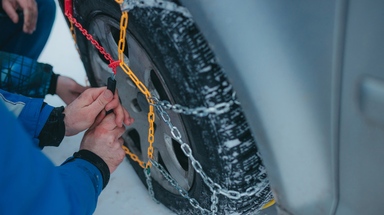 Two people installing snow chains around a car tire