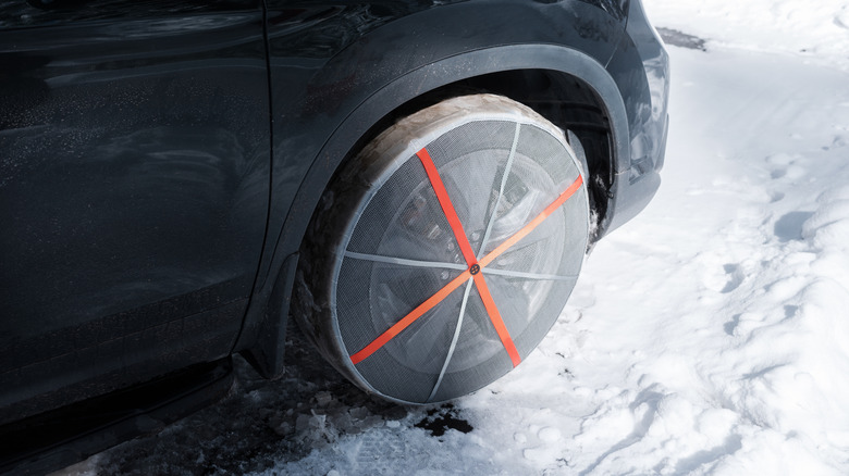 A vehicle's front right wheel with a snow sock installed over the tire