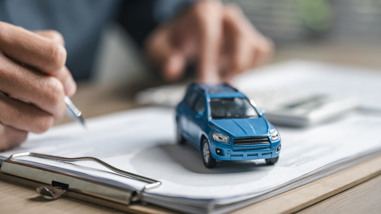 Car purchase concept with contract signing, showing vehicle agreement, insurance coverage, auto loan planning, and financial responsibility during dealership buying and ownership transfer.